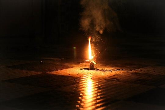 Burning Firecracker Sparking Flame on Floor with Smoke and Light Reflection in Dark Room; Dramatic Celebration Ground Firework Concept Background for Festivals