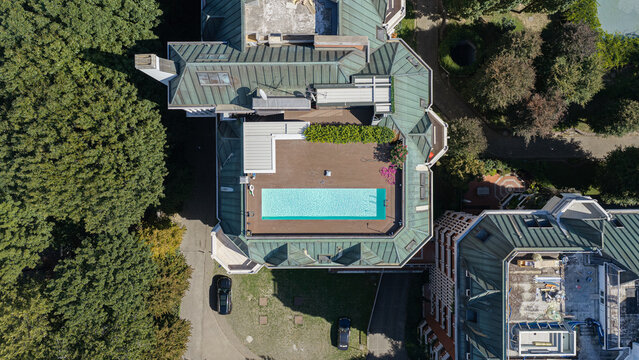 Aerial view of a luxury villa featuring a rooftop swimming pool, green copper roof, and surrounding lush gardens in Milan, Lombardy, Italy.