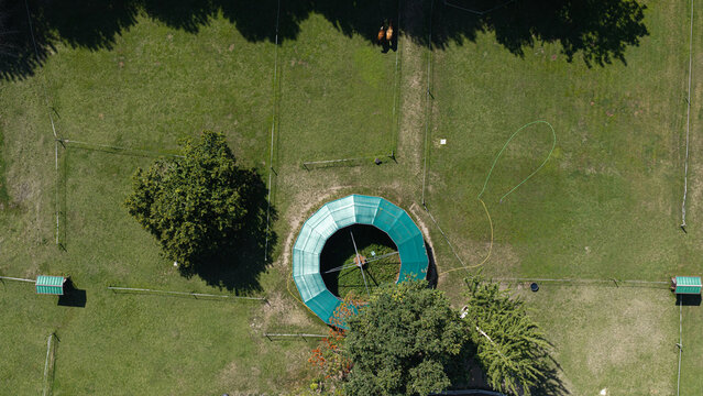 Aerial view of a circular horse walker in a green pasture with trees and horses in Milan, Lombardy, Italy.