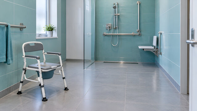 Accessible bathroom with commode chair, disability shower, grab rail and seat for safe hygiene and independent mobility.