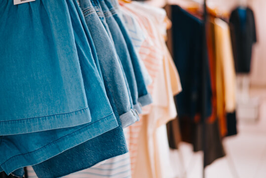 A variety of clothing items, including skirts and shirts, hang on display racks inside a retail store. The fabrics feature different colors and patterns, showcasing the latest fashion styles