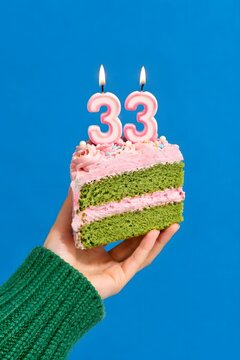 Slice of green cake with pink frosting and lit number 33 birthday candles