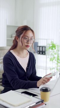 Young Asian businesswoman using calculator while working on laptop in bright modern office space