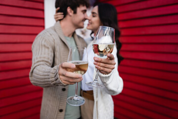 Naklejka premium Joyful couple celebrates love with wine glasses near a cozy red house 