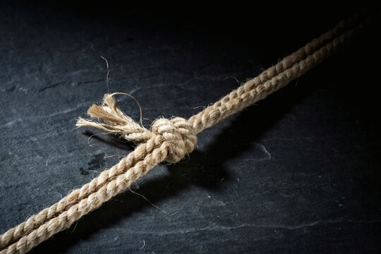 Frayed hemp rope tied in a tight knot on dark slate with loose fibres