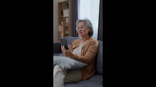 Cheerful senior woman using smartphone while relaxing comfortably on sofa at home, enjoying digital entertainment, communication and independent retirement life.