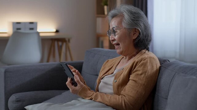 Senior woman relaxing on sofa while browsing smartphone at home, using mobile technology for digital content, communication and leisure during independent retirement life