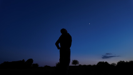 Silhouette of a person in nature observing night sky, Moon, stars and planets from a remote location. © astrosystem