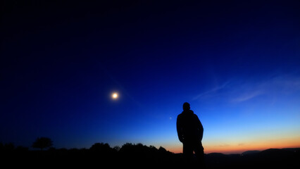 Silhouette of a person in nature observing night sky, Moon, stars and planets from a remote location. © astrosystem