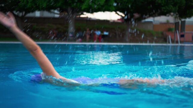 Determined female swimmer performing the backstroke in a clear blue pool. An athletic woman in a swimsuit, cap, and goggles training for a competition with powerful arm strokes