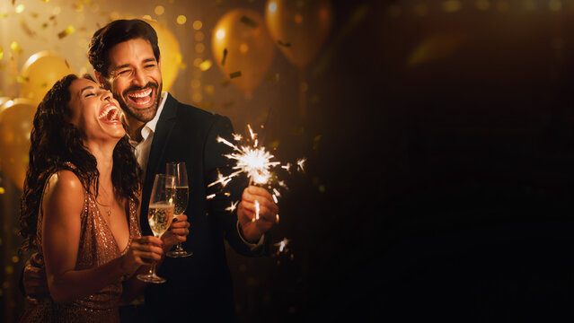 Ecstatic couple celebrating with champagne and sparkler with blurred party background banner.