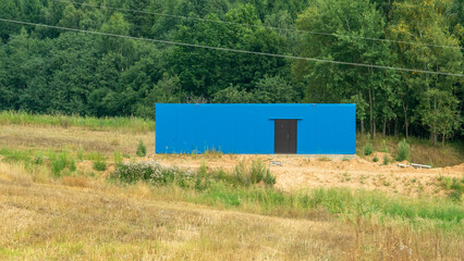 In the serene countryside, a striking blue building stands proudly on a level expanse, framed by lush trees in the background © Сергей Семенов