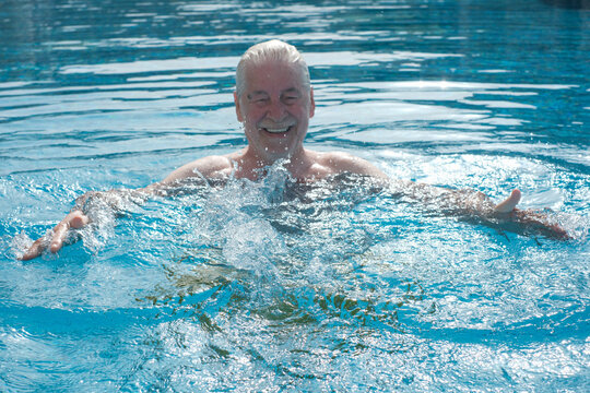Senior man happily splashing in a swimming pool, enjoying leisure time and active lifestyle, finding joy and vitality in summer water activity