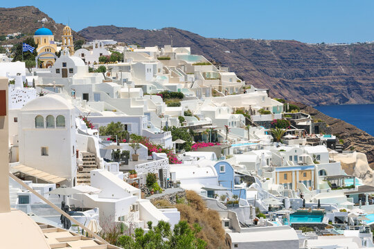 View of Santorini, Greece with blue dome churches and cliff views of houses and businesses overlooking the caldera. Famous tourism destination.