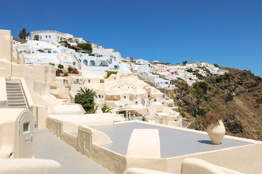 View of Santorini, Greece with blue dome churches and cliff views of houses and businesses overlooking the caldera. Famous tourism destination.