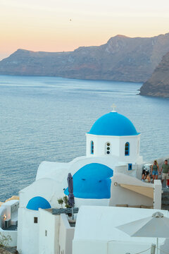 View of Santorini, Greece with blue dome churches and cliff views of houses and businesses overlooking the caldera. Famous tourism destination.