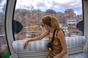 Woman rides the Metrocable gondola over the colorful hillside neighborhoods of Medellin, Colombia, taking in the view during a modern urban travel adventure © Gonzalo