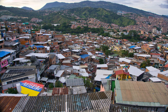 Elevated view over the densely packed rooftops of Comuna 13 in Medellin, Colombia, at dusk, showcasing the vibrant urban transformation of this once-troubled neighborhood