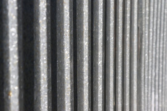 Close-up view of a weathered corrugated metal surface with parallel vertical ridges, industrial texture and subtle metallic highlights.