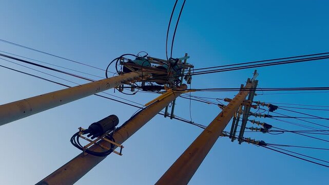 Video of the view of the electric pole from the bottom angle showing the moving cable blown by the wind, with the background of the blue sky in the afternoon