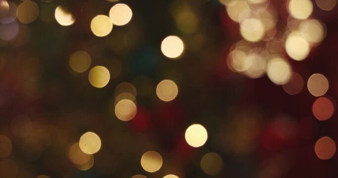 Bokeh lights glowing in dark festive environment, blurred Christmas tree background, defocused golden and red circles, holiday celebration atmosphere.