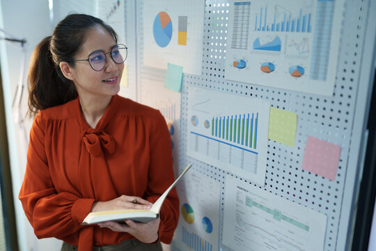 Professional businesswoman reviewing performance charts and writing notes while analyzing data for strategic planning and business decision-making.
