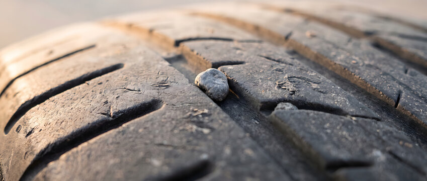 A close-up view of a small stone lodged in the deep tread grooves of a black rubber vehicle tire, showing texture and detail.