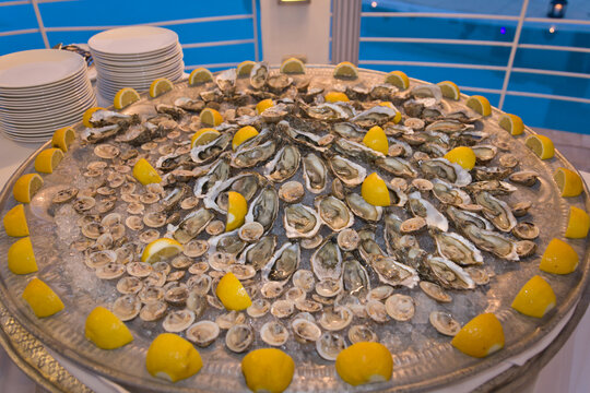 large inviting round plate of fresh oysters of different sizes with lemon garnish against blue pool, cuisine, seafood, reception, party, appetisers