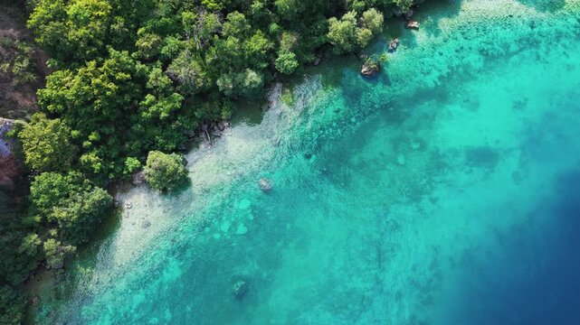 Drone view of a scenic road winding along rocky, forested cliffs and the turquoise waters of Lake Ohrid near Ohrid, North Macedonia. Natural shoreline, secluded beach and clear water on a sunny summer