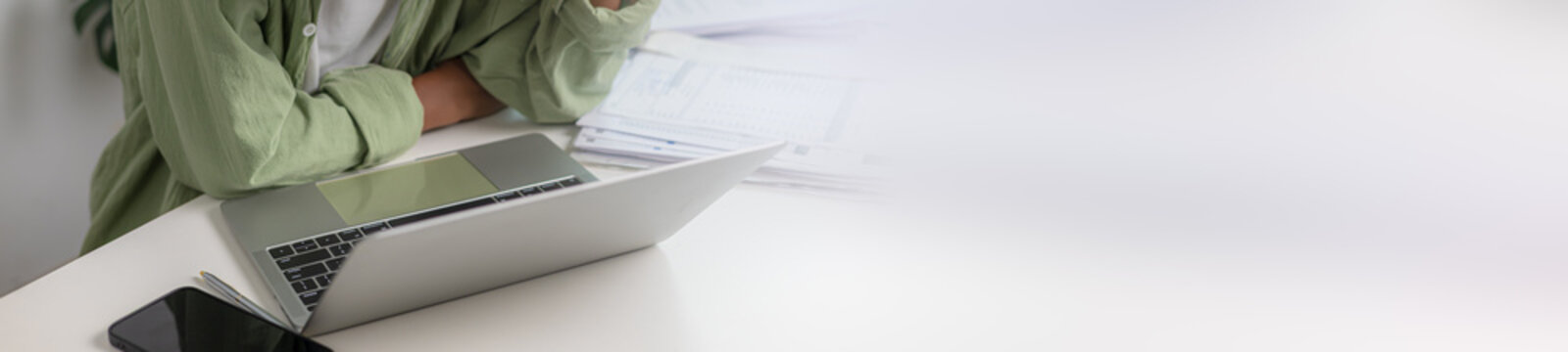 Cropped shot of a businessman working on a laptop at a white office desk with papers and smartphone, featuring a wide blank copy space banner background for design text overlay.