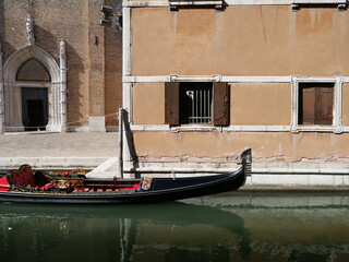 a still venetian gondola boat on a canal in Venezia (Venice), Italy,  in front of a building and a church © Isabella