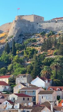 Fortress on a hill overlooking a coastal town with traditional architecture and greenery in the foreground in Hvar, Croatia 