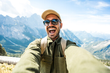 Fototapeta premium Young hiker man taking selfie portrait on the top of mountain - Smiling man enjoying summer vacations with italian alps on background