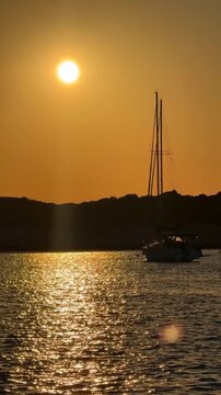 View from bow of sailing yacht anchored in quiet bay during golden sunset with other boats in distance. Concept of slow travel, sailing adventure, anchoring, freedom and peaceful evenings on water