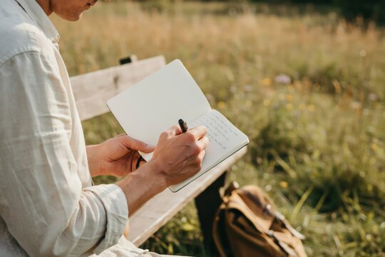 Man writing in a notebook while sitting on a wooden bench in a meadow
