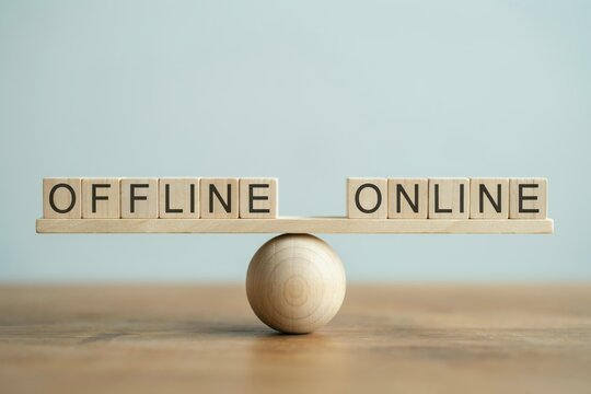 Wooden blocks with the words offline and online balancing on a wooden scale