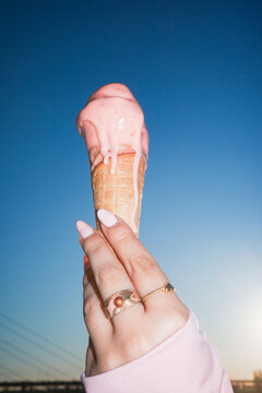 Melting strawberry cone raised toward blue sky