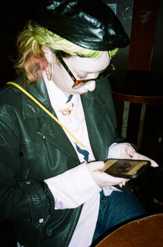 Green-haired person scrolling phone in a dark bar