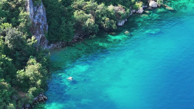 Drone view of a scenic road winding along rocky, forested cliffs and the turquoise waters of Lake Ohrid near Ohrid, North Macedonia. Natural shoreline, secluded beach and clear water on a sunny summer