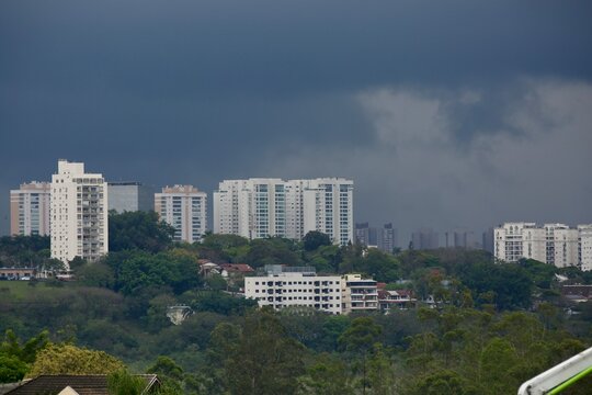 Fundo preto do ceu com chuvas intensas e predios urbanos ao redores.