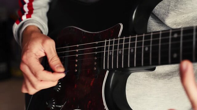 Strumming electric bass guitar. Musician plays music. Man fingers holding mediator. Man hand playing guitar neck in dark room