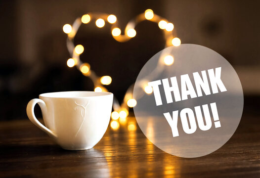Thank you message with a warm cup of coffee and heartshaped string lights on table