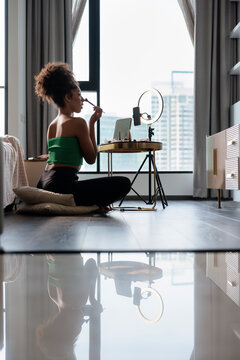 Young woman applying make up while streaming