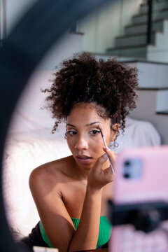 A woman applying makeup while filming a video tutorial