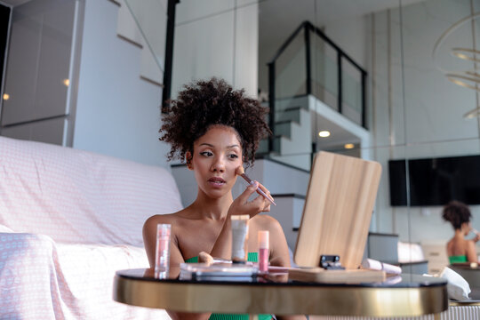 Young woman applying makeup at her home vanity