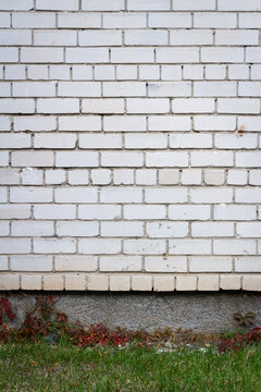 Old cracked white brick wall with green grass. Architectural detail background.