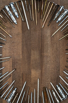 Circle made of various screws and nails on brown wood texture. Industrial flat lay. Carpentry still life.