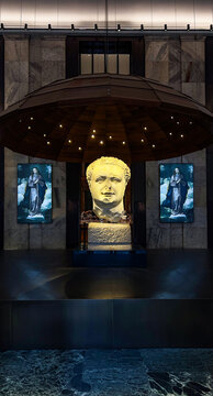 A large classical stone sculpture head displayed under a suspended dome structure with embedded lights in a museum.