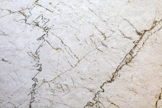 White Marble Texture with Fine Dark Natural Veins. Close-up of white marble stone with fine dark veins, cracks, and subtle natural texture.