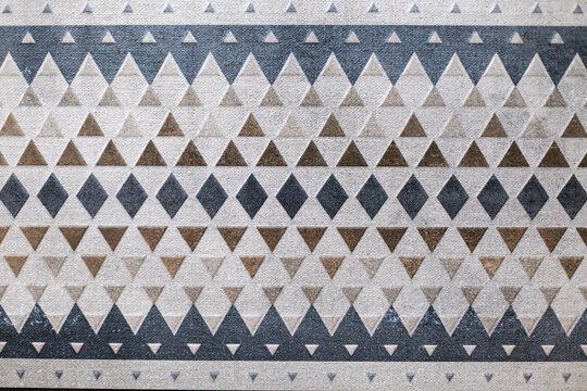 Geometric Triangle and Diamond Pattern in Neutral Tones. Close view of a neutral geometric pattern with repeating triangles and diamonds in beige, brown, gray, and black.